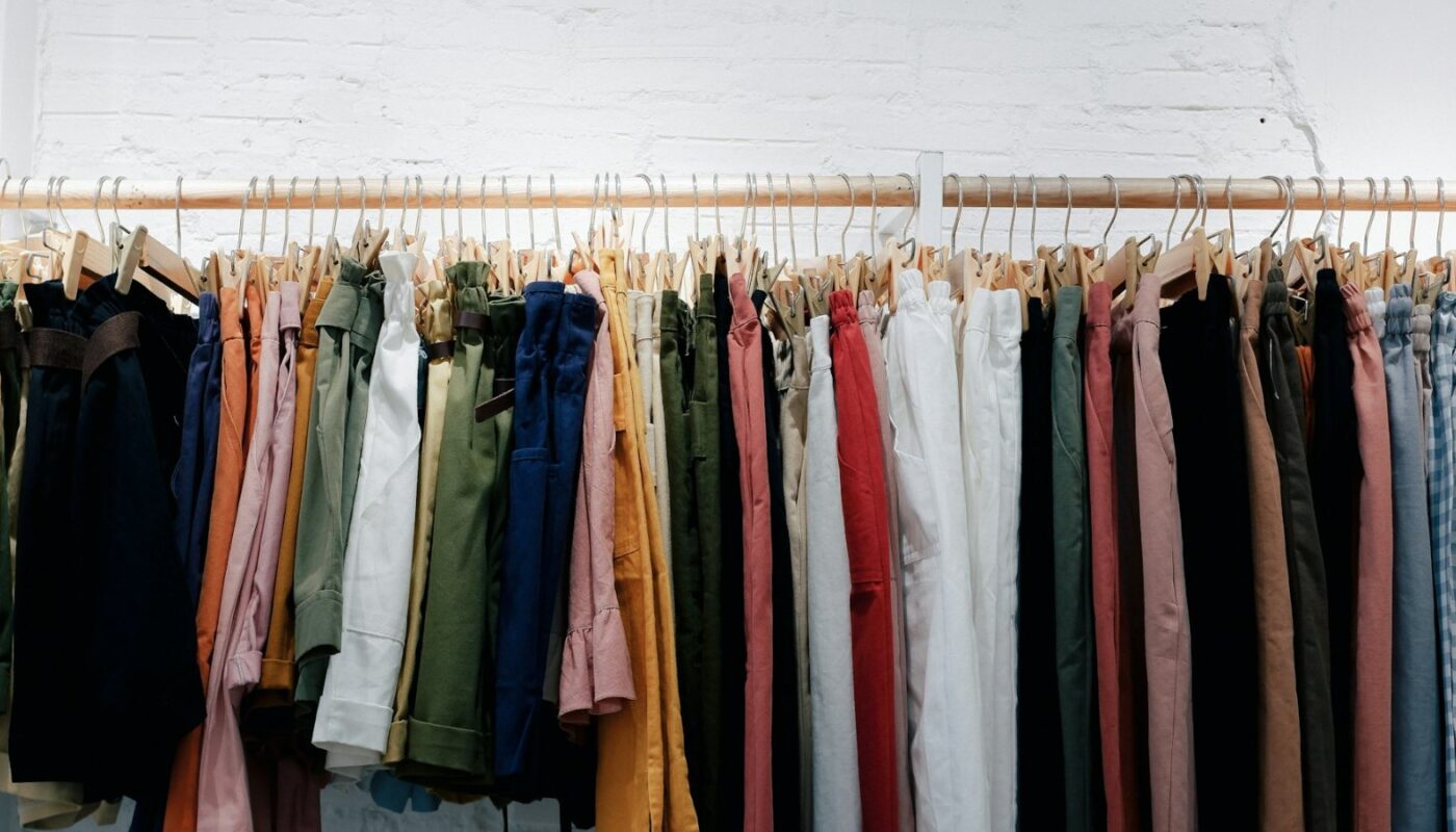 Assorted clothes hanging on a wooden wall-mounted rack (photo: Fujiphilm / Unsplash)