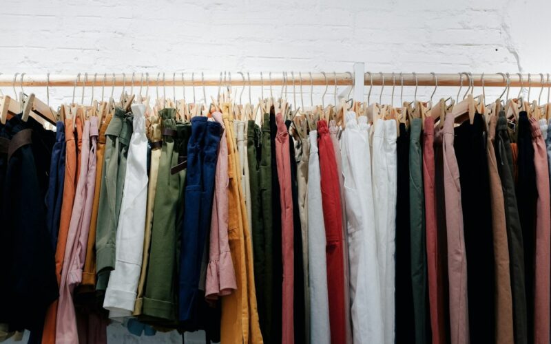 Assorted clothes hanging on a wooden wall-mounted rack (photo: Fujiphilm / Unsplash)
