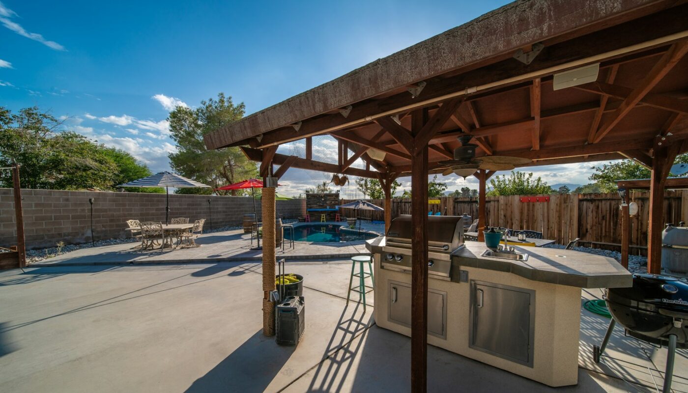 A covered outdoor kitchen with a built-in grill beside a backyard pool (photo: Brian Wangenheim / Unsplash)