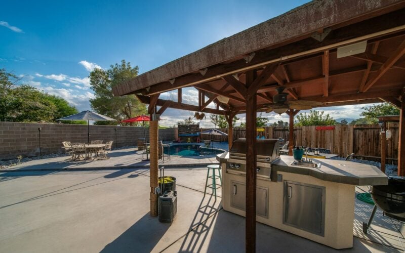 A covered outdoor kitchen with a built-in grill beside a backyard pool (photo: Brian Wangenheim / Unsplash)