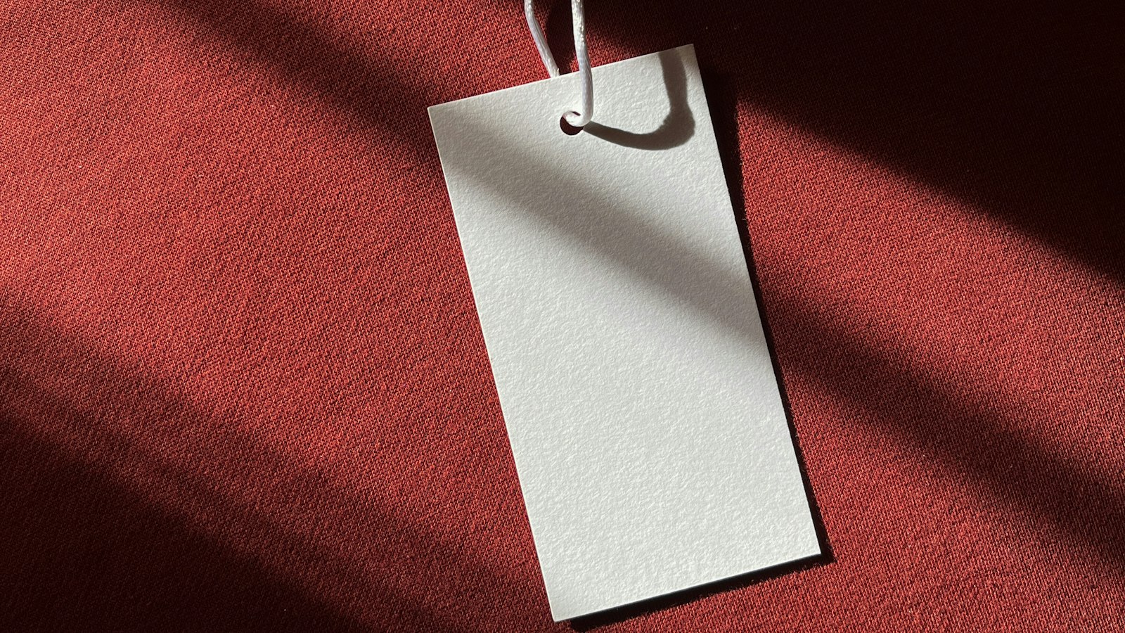 A blank white swing tag resting on red fabric in raking light (photo: Anastasiya Doicheva / Unsplash)