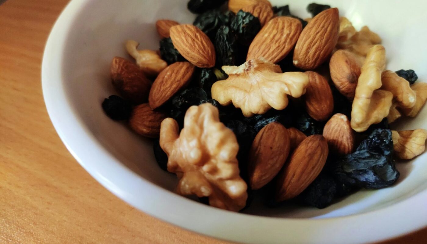 White bowl of almonds, walnuts and dried fruit on a wooden table