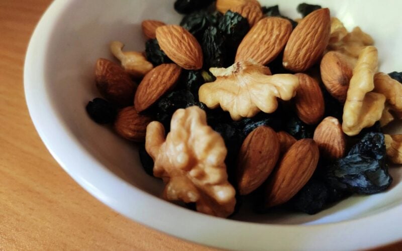 White bowl of almonds, walnuts and dried fruit on a wooden table