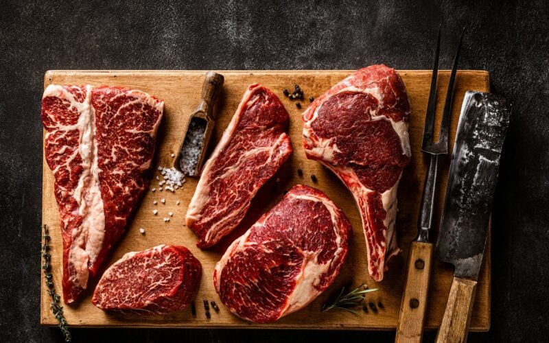 Raw marbled steaks on a wooden board with a knife and fork (photo: Sergey Kotenev / Unsplash)