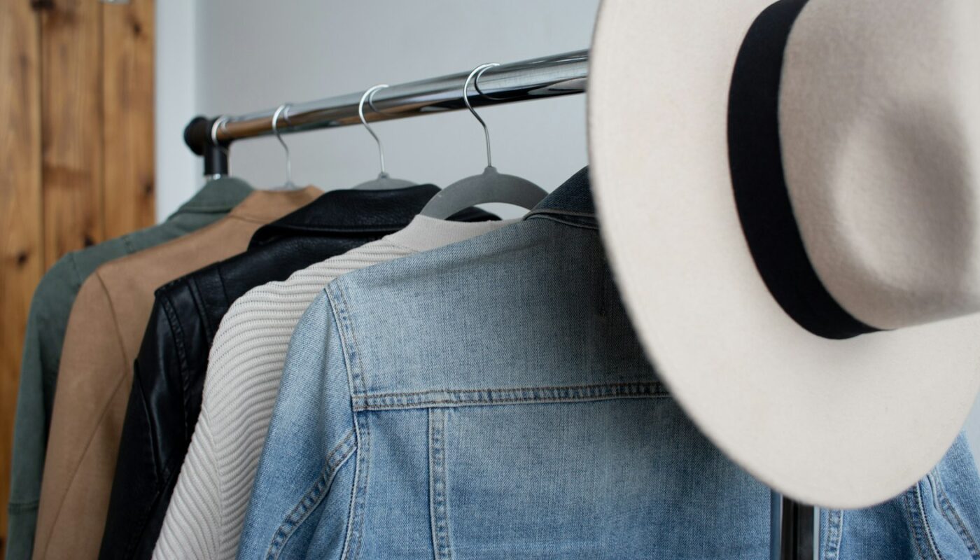 Jackets and knitwear hanging on a clothing rail beside a wide-brimmed hat (photo: Amanda Vick / Unsplash)