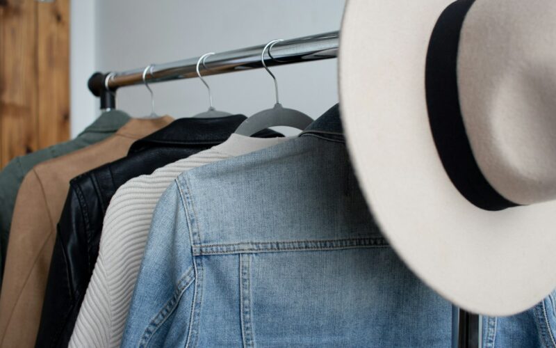 Jackets and knitwear hanging on a clothing rail beside a wide-brimmed hat (photo: Amanda Vick / Unsplash)