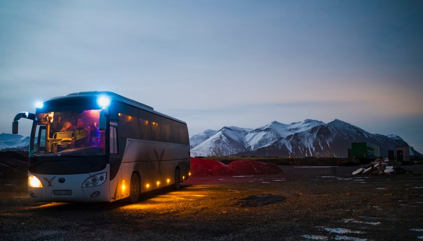 A white and black coach driving on a highway near mountains (photo: Juan Encalada / Unsplash)