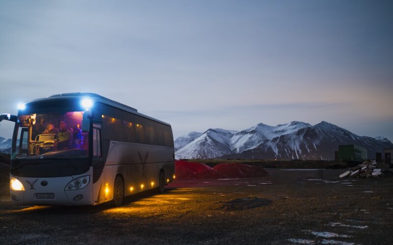A white and black coach driving on a highway near mountains (photo: Juan Encalada / Unsplash)
