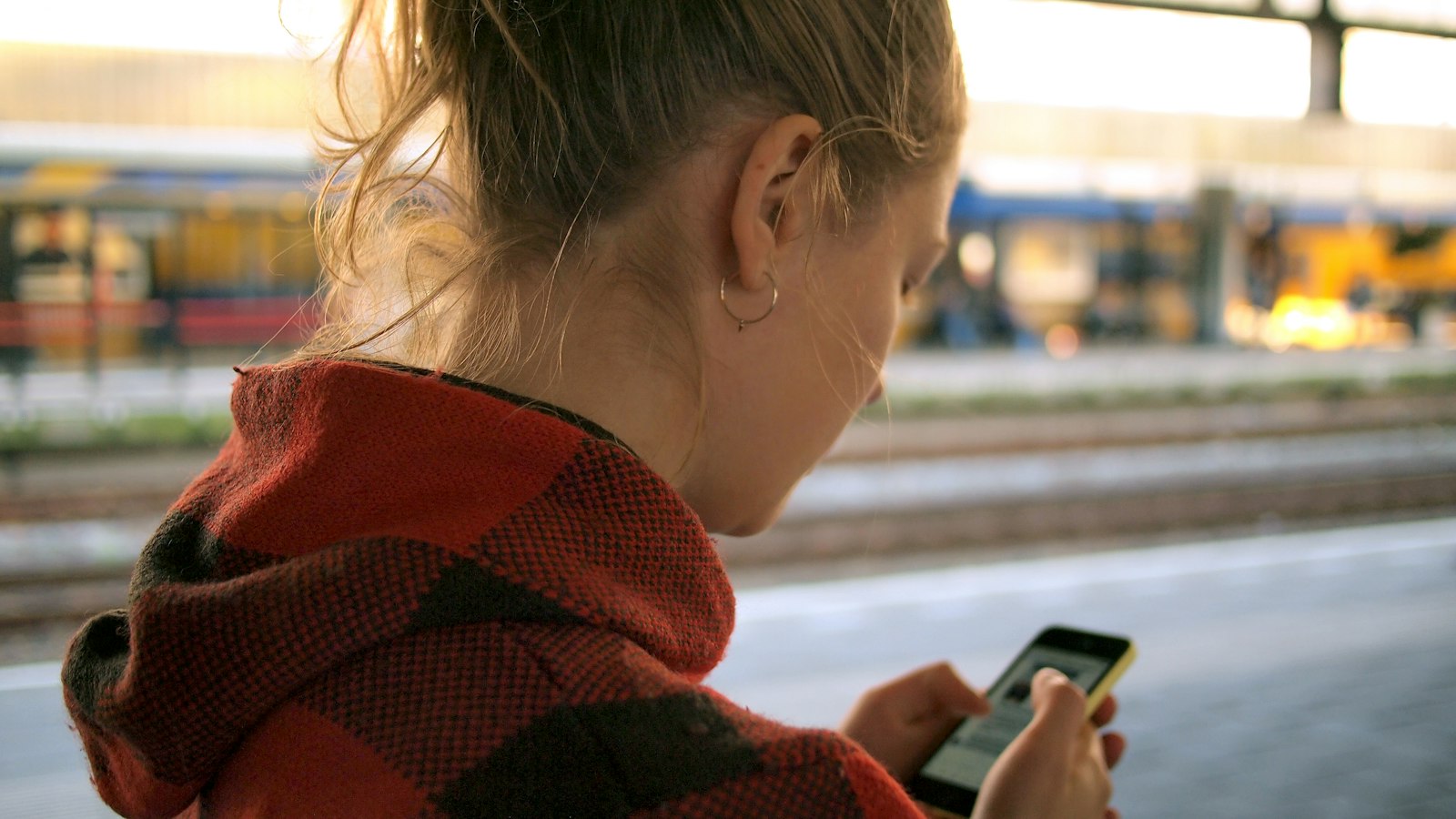 Woman watching her phone on a train platform (photo: Daria Nepriakhina / Unsplash)