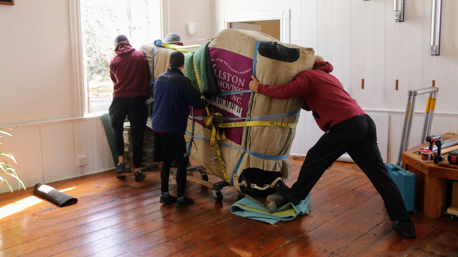 Three people manoeuvring a large wrapped item through the inside of a home