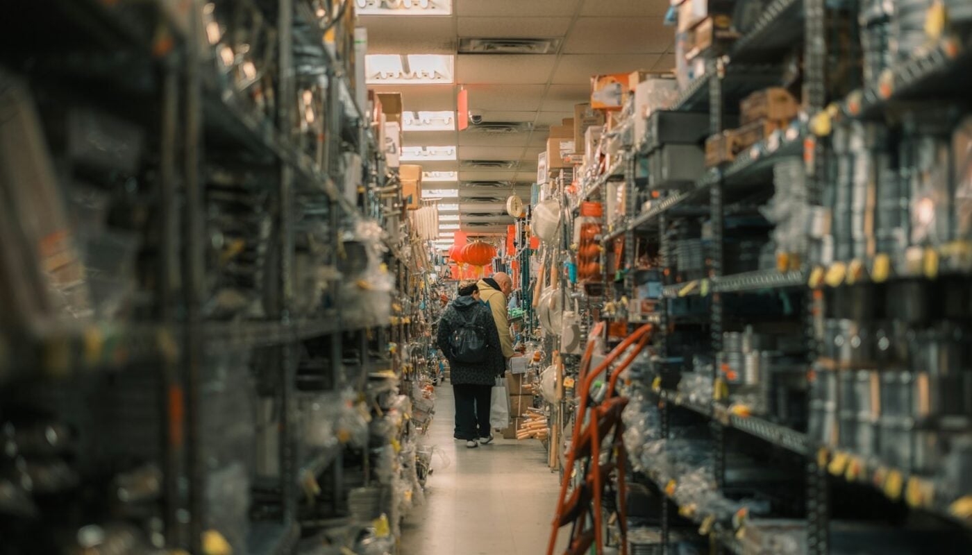 A lone shopper walking down a narrow store aisle lined floor to ceiling with stock (photo: Tianlei Wu / Unsplash)