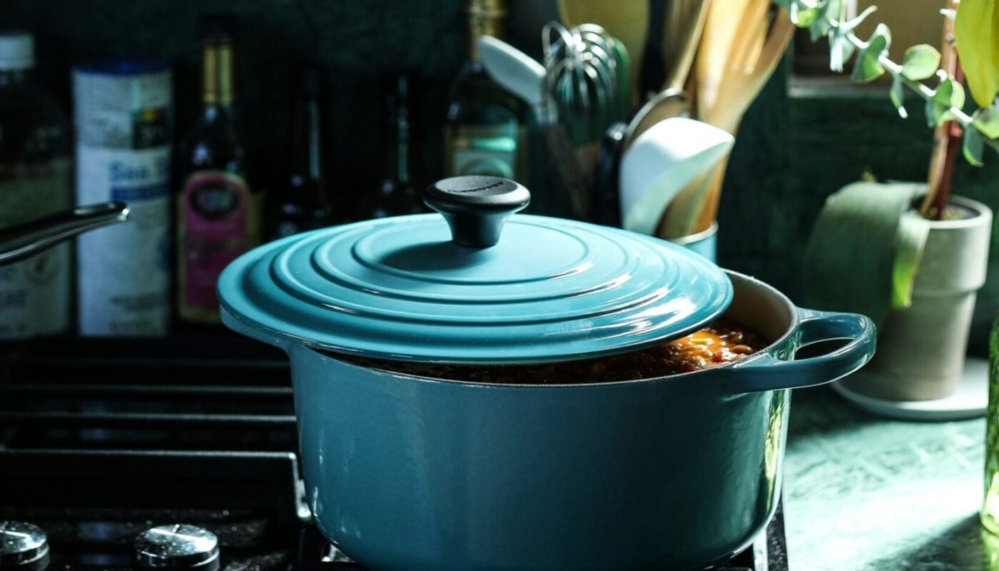Teal enamelled cast-iron Dutch oven simmering on a gas hob in a dark green kitchen