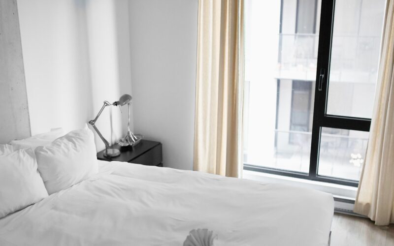 An empty white hotel bed beside a window (photo: Andrew Neel / Unsplash)