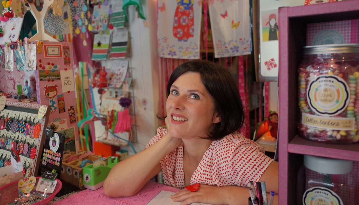 A smiling shop owner behind the counter of a colorful gift shop (photo: Remy Baudouin / Unsplash)