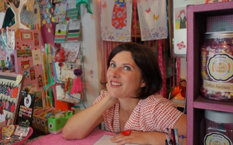 A smiling shop owner behind the counter of a colorful gift shop (photo: Remy Baudouin / Unsplash)