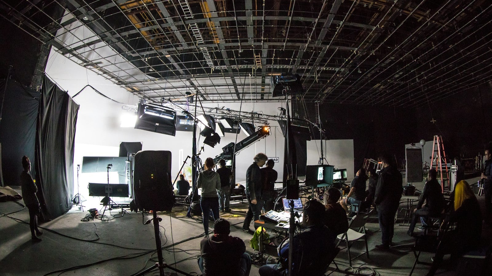 A large film crew and lighting rig set up around a white cyclorama on a sound stage