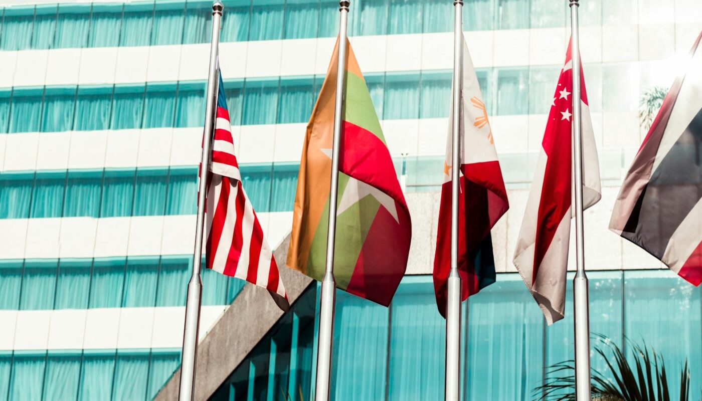 Flags of several countries flying in front of a glass office building (photo: Kaung Myat Min / Unsplash)