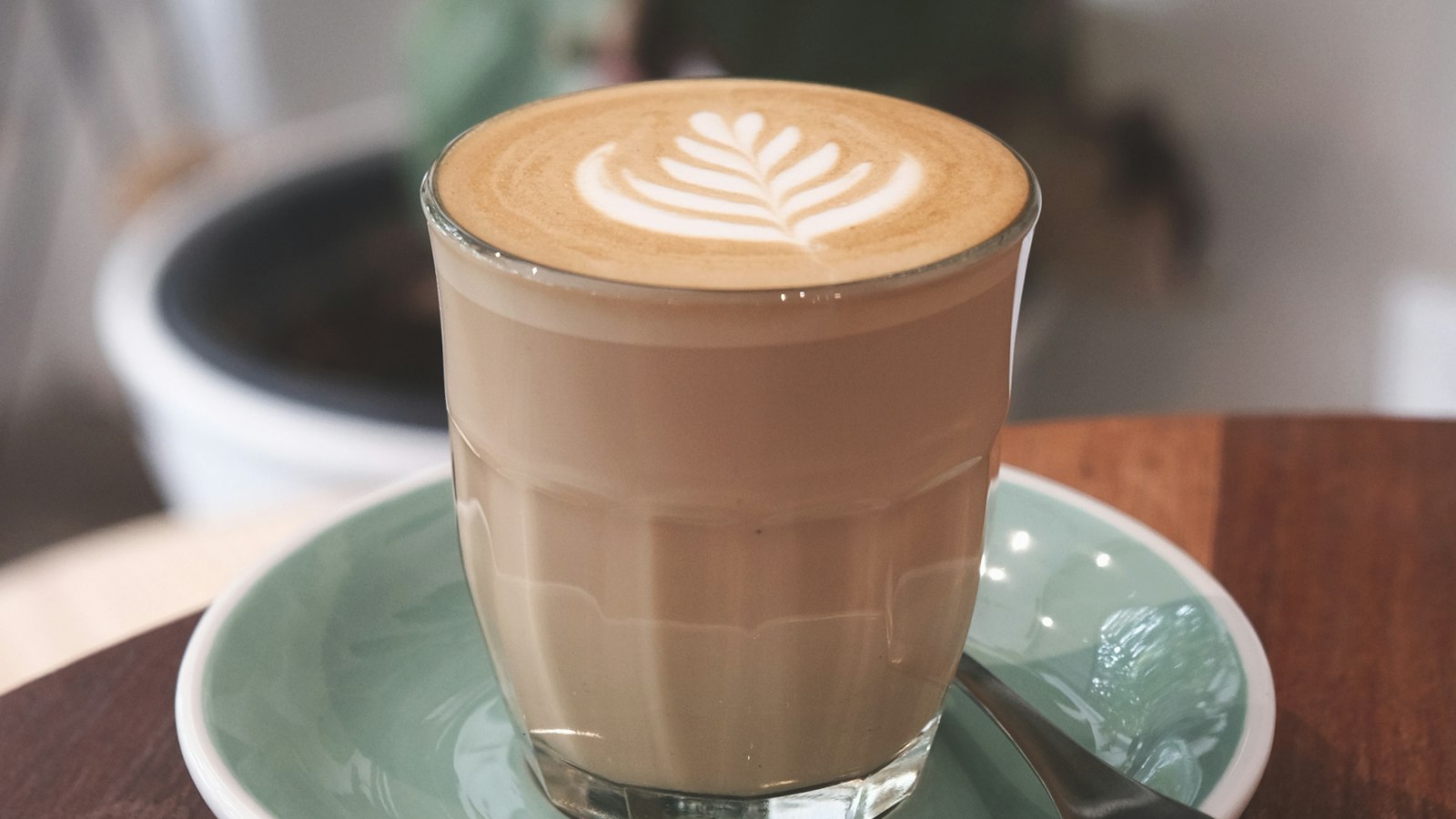 A flat white with latte art in a glass on a green saucer on a café table (photo: Lex Sirikiat / Unsplash)