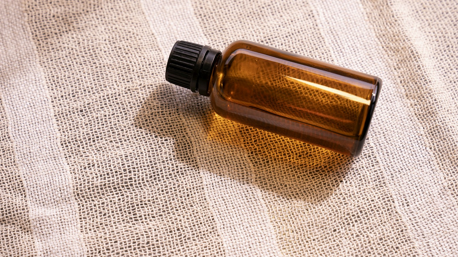 An amber glass bottle with a black cap lying on gauze fabric (photo: Denise Chan / Unsplash)