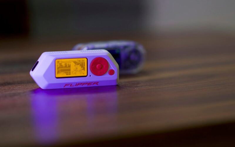 A Flipper Zero multi-tool device resting on a wooden desk with its screen lit
