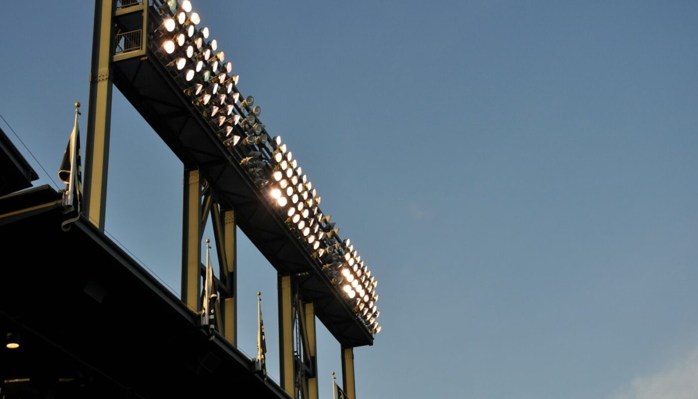Stadium floodlight gantry lit against a dusk sky (photo: Marta Serrano / Unsplash)