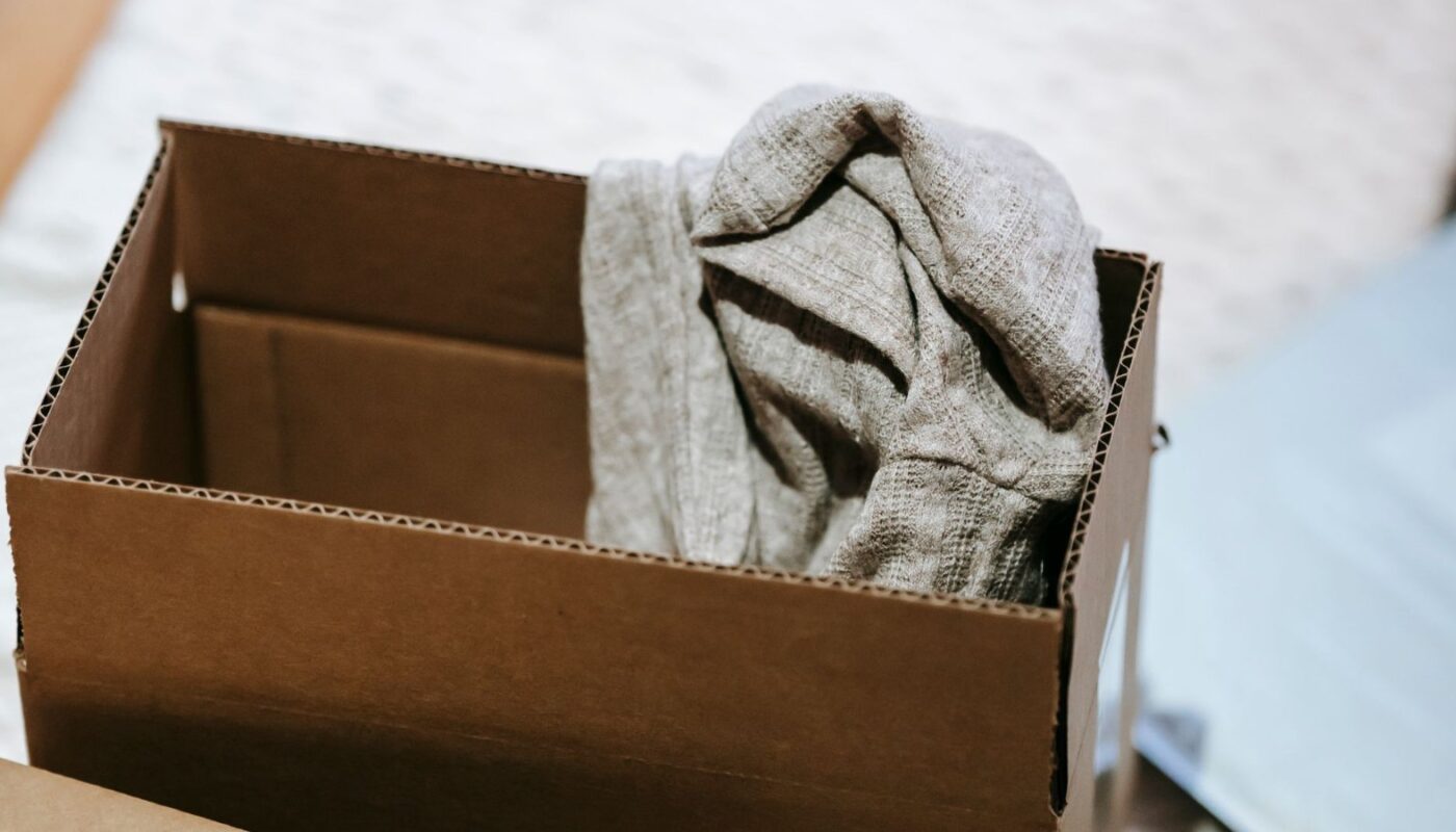A folded knitted jumper packed inside an open cardboard shipping box