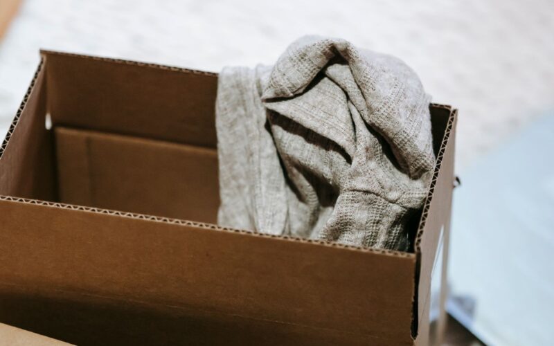 A folded knitted jumper packed inside an open cardboard shipping box