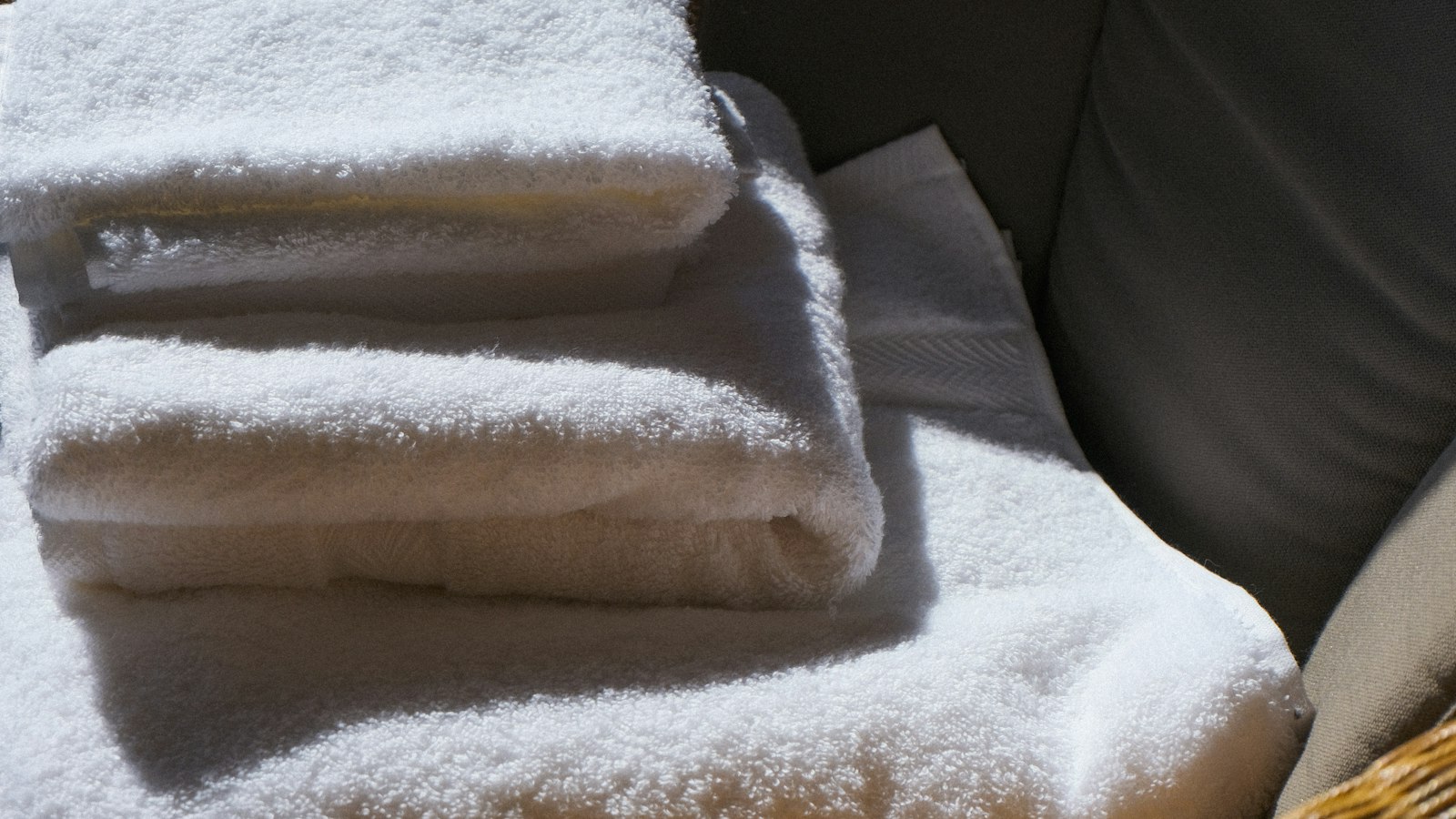 A stack of fresh, folded white towels on a grey sofa (photo: Mads Leif Hansen / Unsplash)