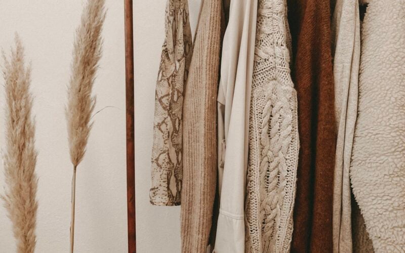 Neutral knitwear and jackets hanging on a rail beside dried pampas grass (photo: Alyssa Strohmann / Unsplash)