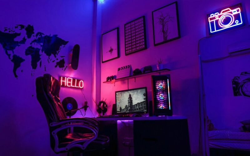 A gaming room lit in purple and pink neon with a desk setup (photo: Chuck Fortner / Unsplash)