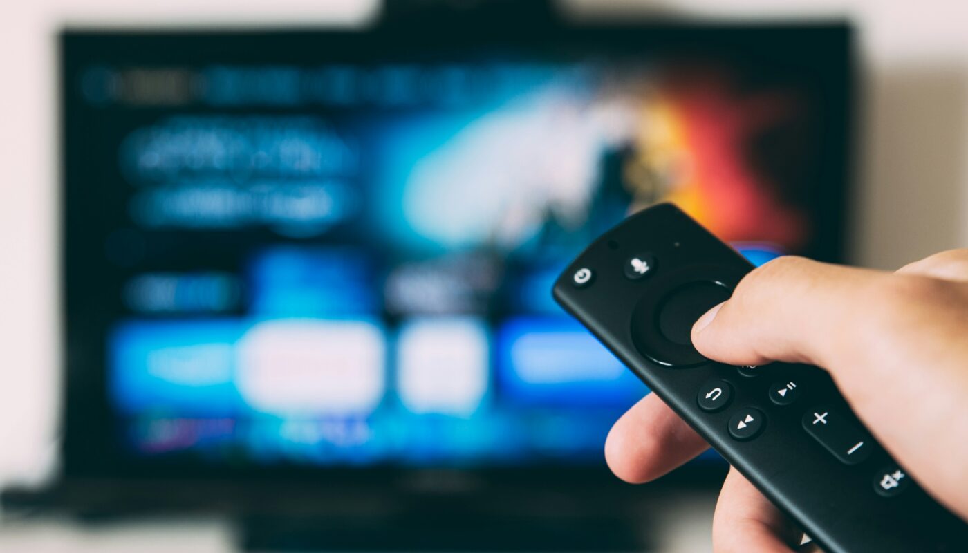 Hand holding a remote control pointed at a blurred television menu