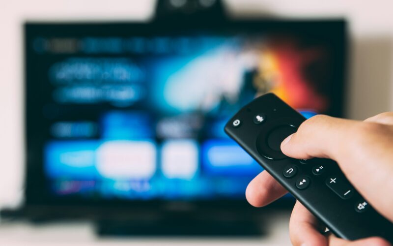 Hand holding a remote control pointed at a blurred television menu