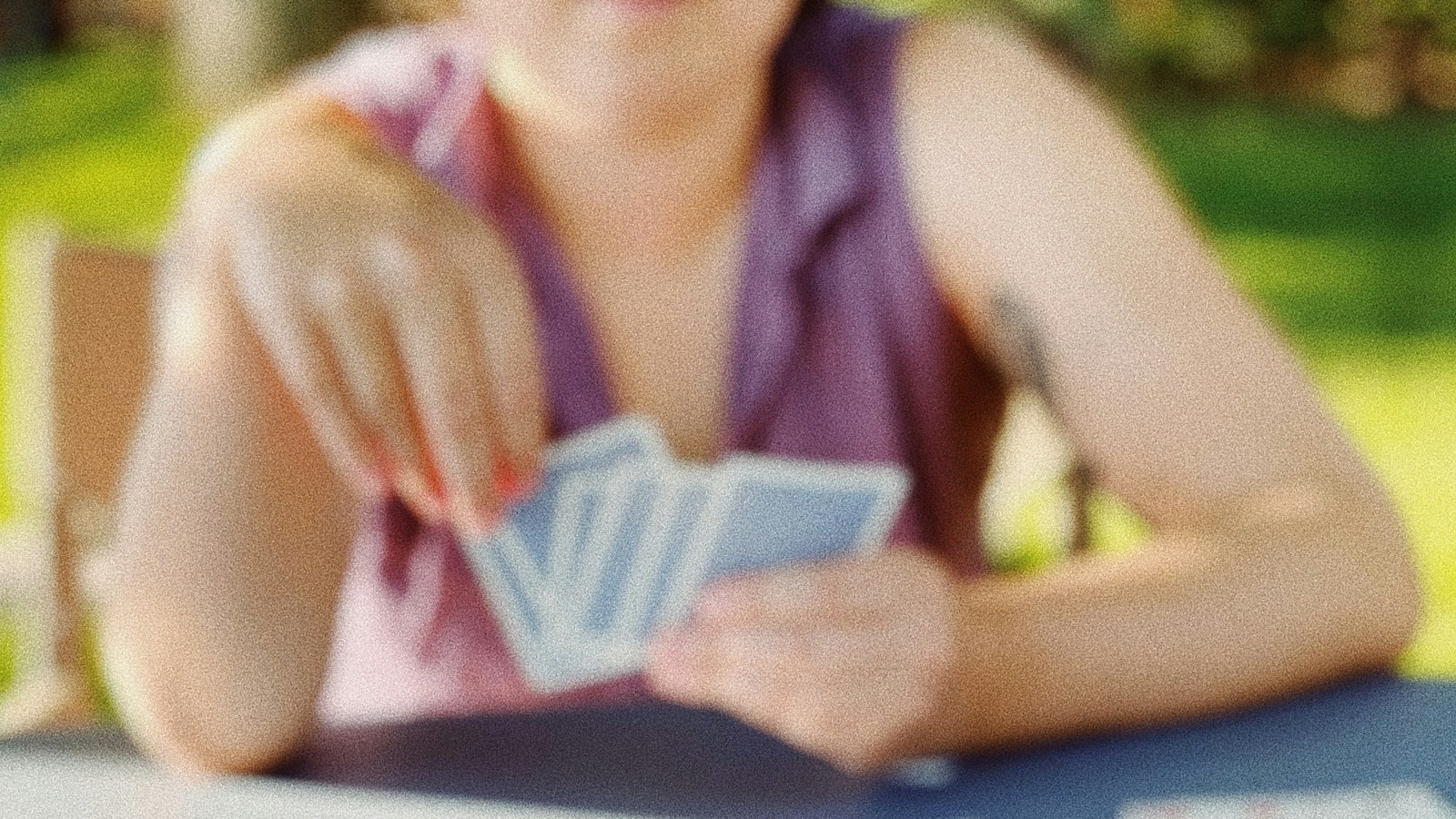 A player holding a hand of playing cards over a table (photo: Meg Jenson / Unsplash)