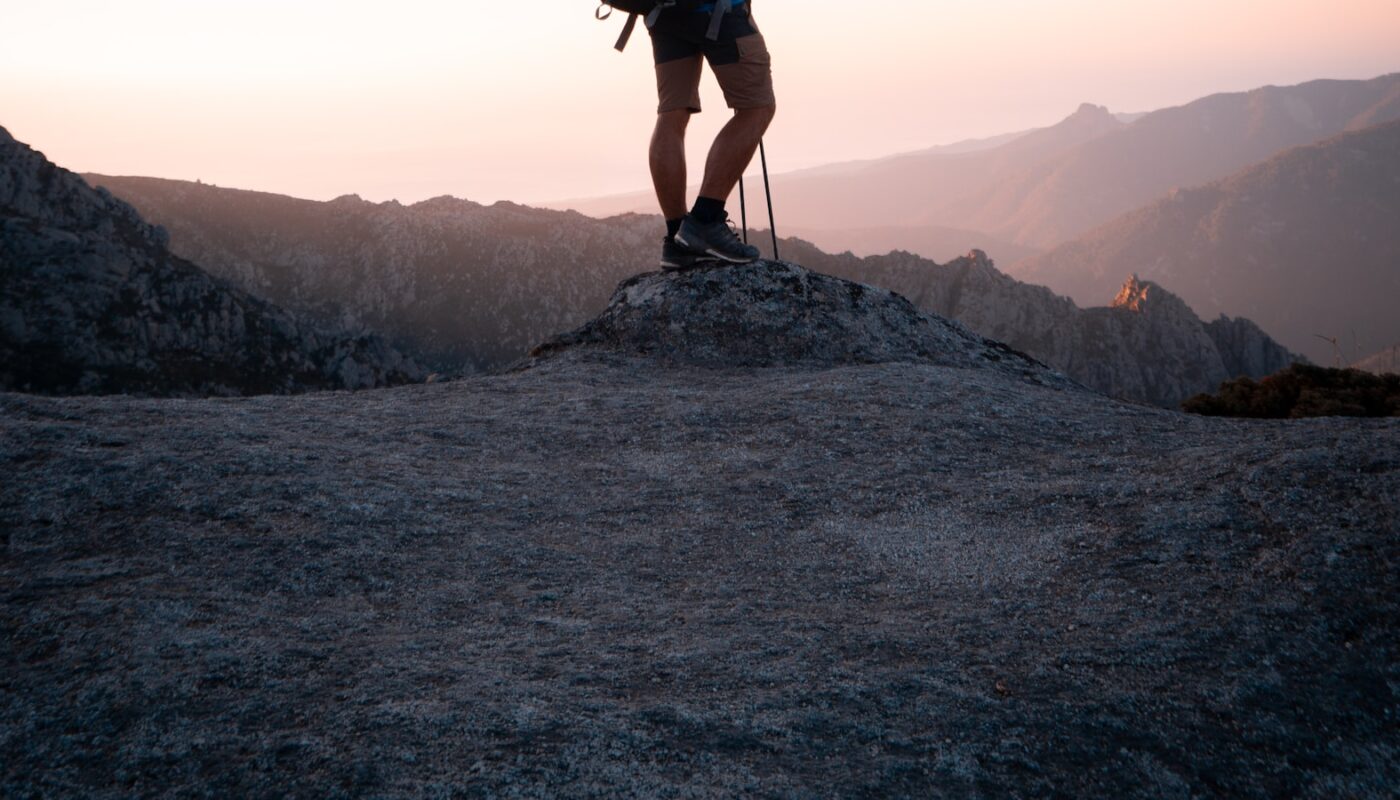 A hiker carrying a large backpack standing on a rocky ridge at dusk (photo: lucas Favre / Unsplash)