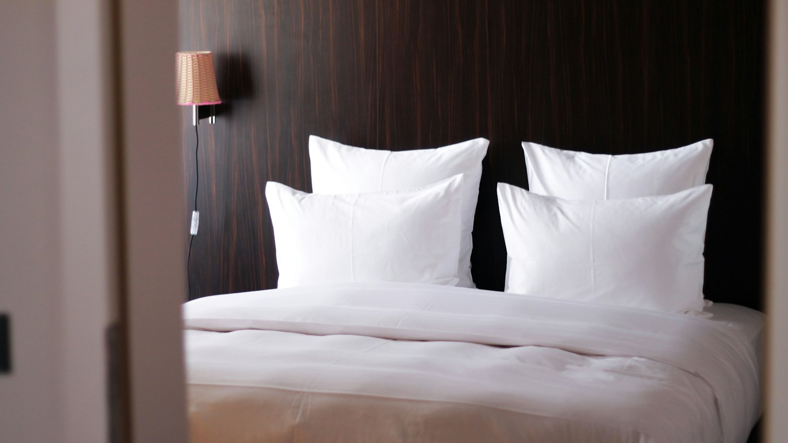 A made-up bed with four crisp white pillows and a white duvet against a dark wood headboard (photo: Dave Photoz / Unsplash)