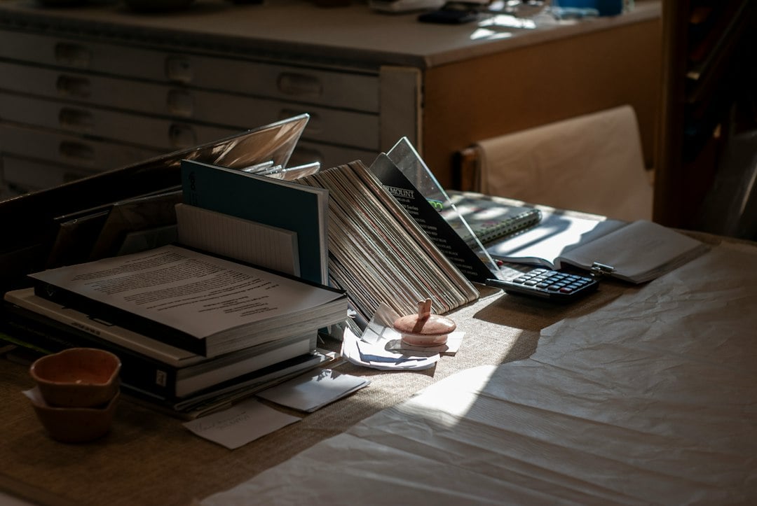 A dimly lit desk piled with documents, files and a calculator