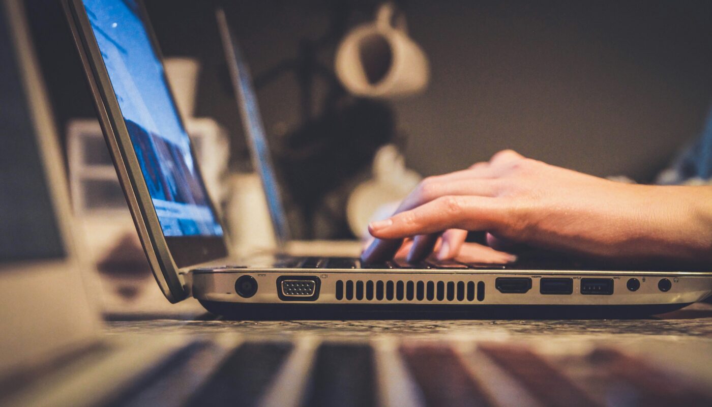 Hands typing on a laptop keyboard with the screen lit
