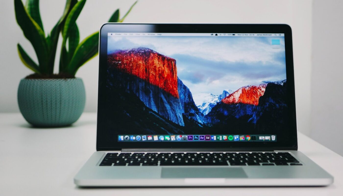 MacBook on a wooden desk beside a plant (photo: James McKinven / Unsplash)
