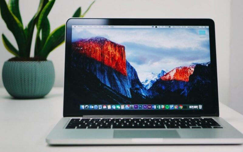 MacBook on a wooden desk beside a plant (photo: James McKinven / Unsplash)