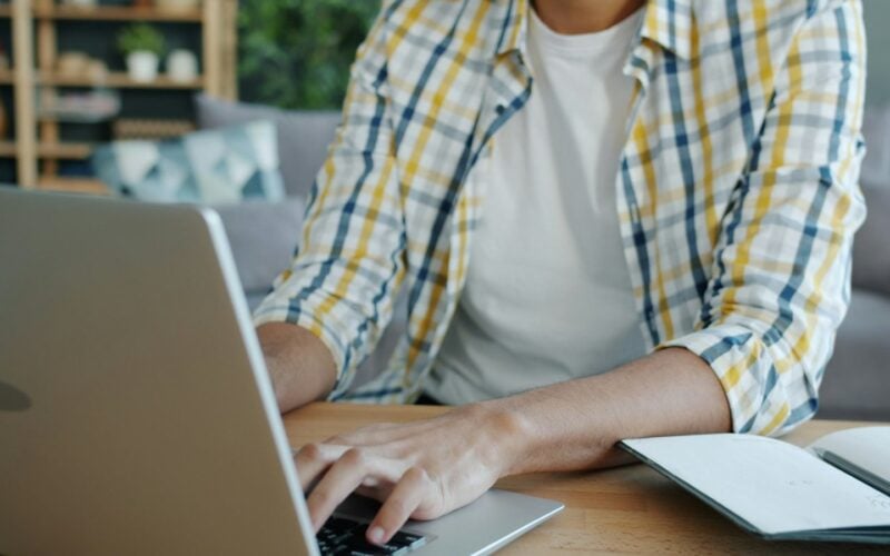 Man typing on a laptop beside an open notebook at a desk (photo: Vitaly Gariev / Unsplash)