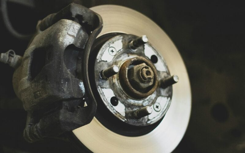 A car brake disc and caliper exposed with the wheel removed (photo: Benjamin Brunner / Unsplash)