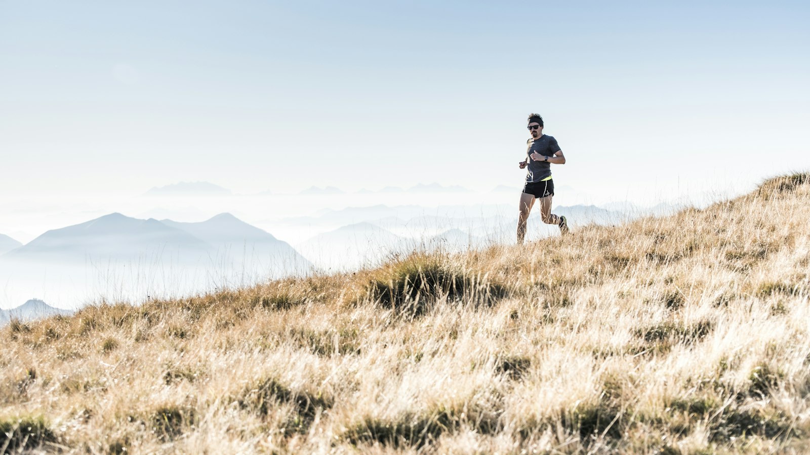 A runner on a grassy ridge above the clouds (photo: Alessio Soggetti / Unsplash)