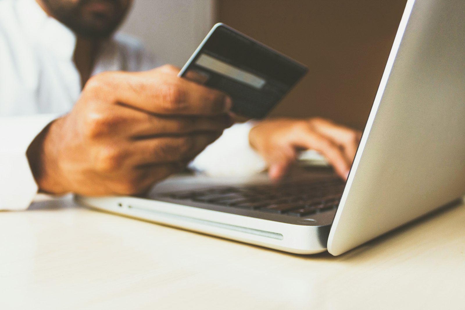 Hand holding a card while shopping online on a laptop (photo: rupixen / Unsplash)