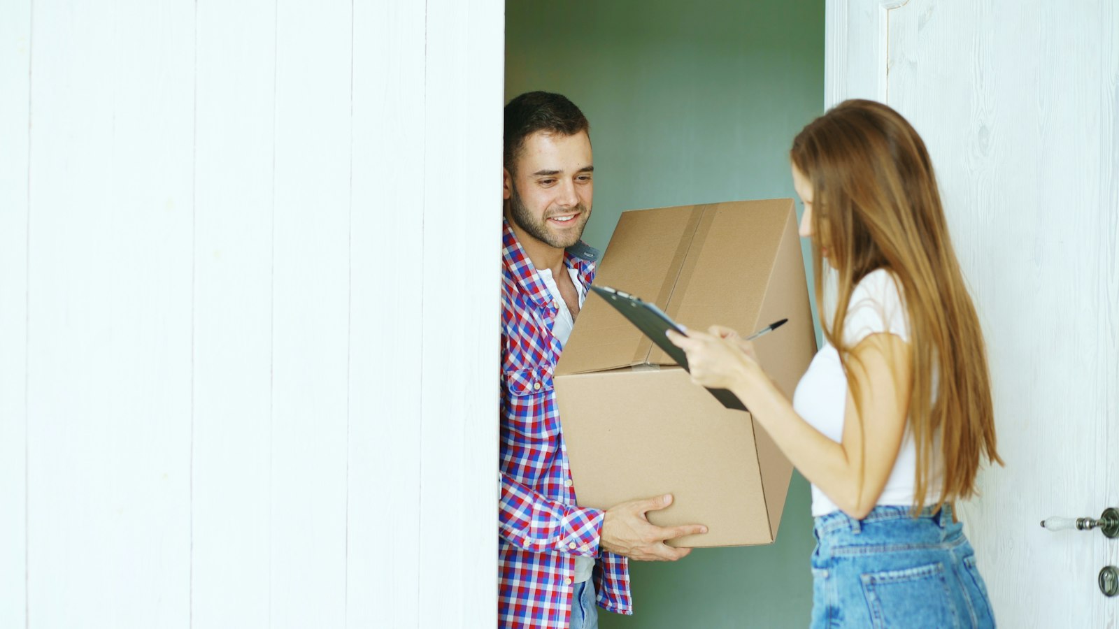 A woman signing for a large cardboard parcel handed over at a front door