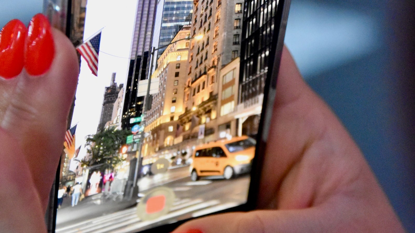 Hands holding a phone up to a busy city street with a taxi passing (photo: Samuel Isaacs / Unsplash)
