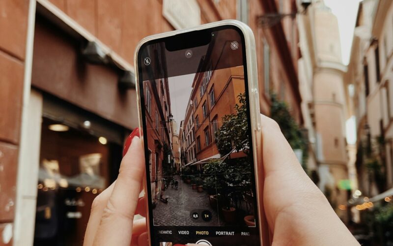 A hand holding a phone up to photograph a narrow European street lined with old buildings (photo: Valentyn Chernetskyi / Unsplash)