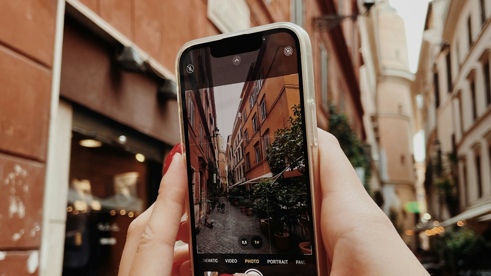 A hand holding a phone up to photograph a narrow European street lined with old buildings (photo: Valentyn Chernetskyi / Unsplash)