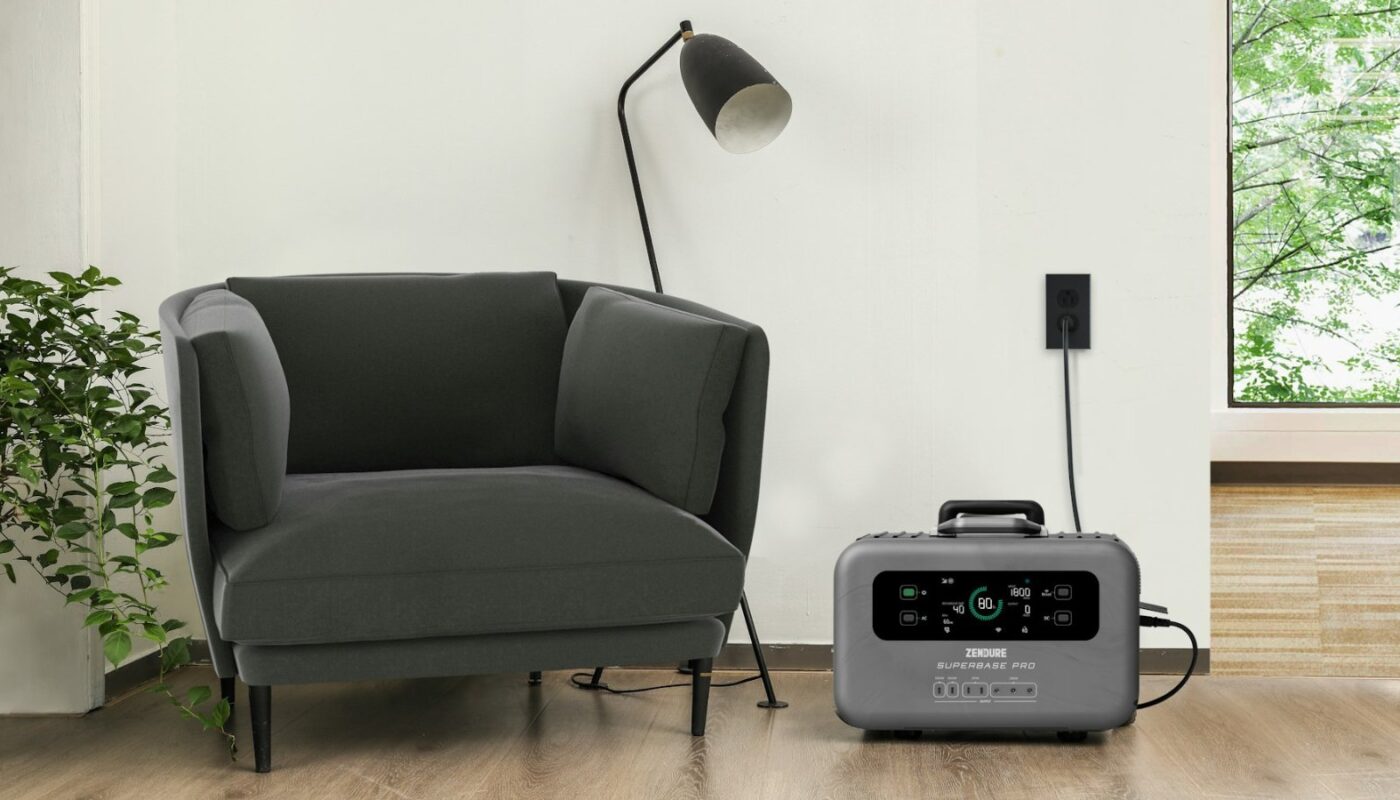 An unbranded grey portable power station charging from a wall outlet in a living room, its display reading 80 percent