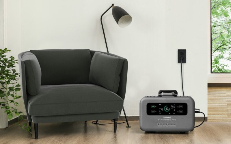 An unbranded grey portable power station charging from a wall outlet in a living room, its display reading 80 percent