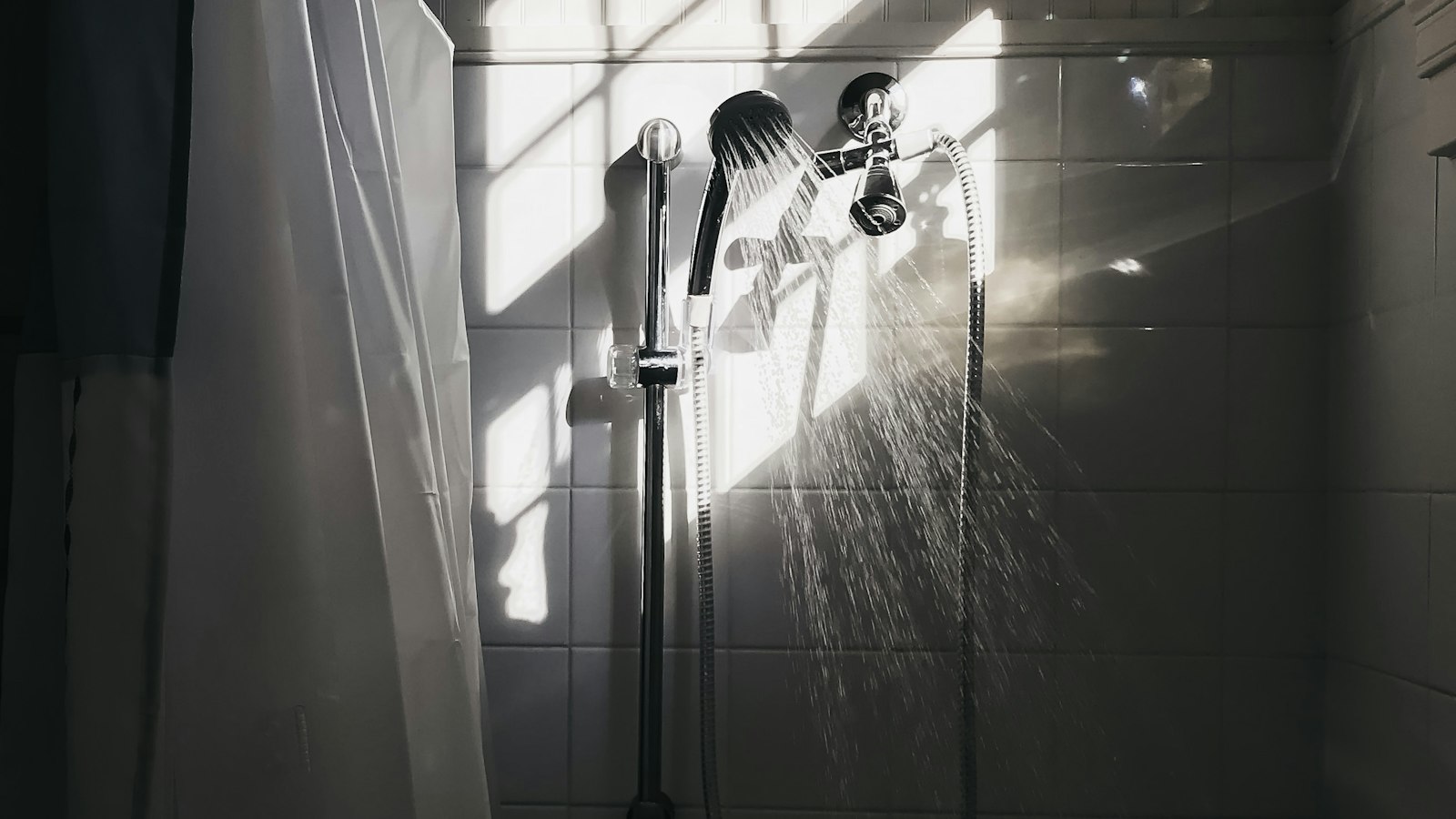 Shower head running water in a tiled bathroom (photo: Tanner Marquis / Unsplash)